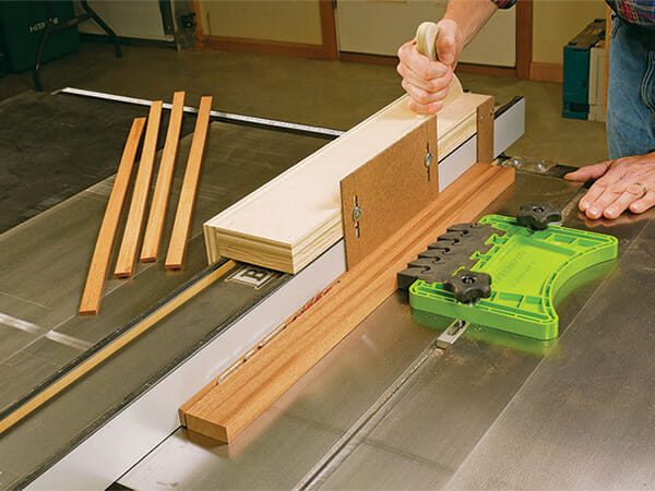  table saw to cut a thin strip of wood with a push stick and featherboard for safety.